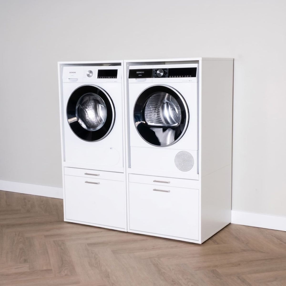 Modern white front-loading washer and dryer set with storage drawers on wood floor against gray wall.